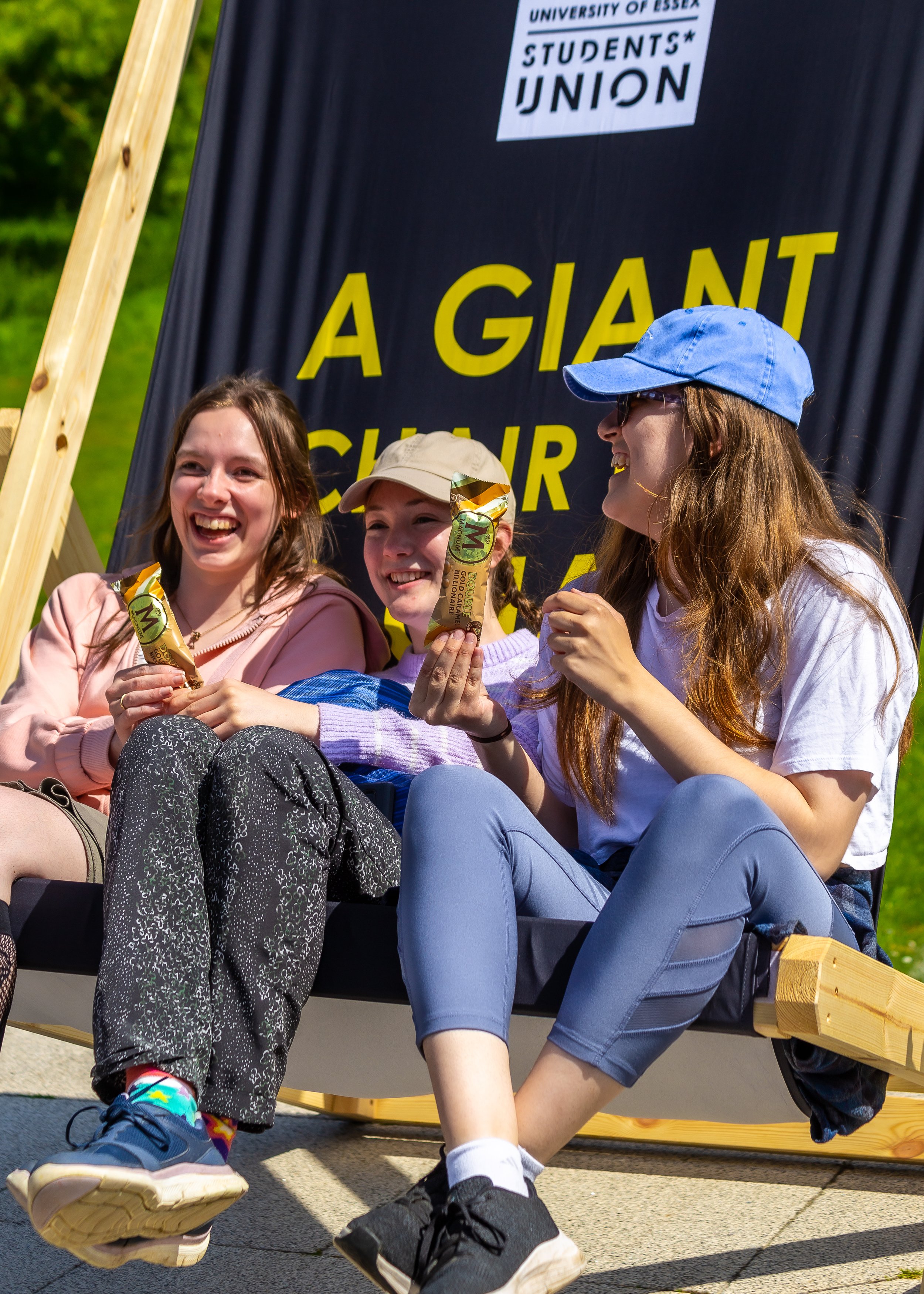 Three students sit on a large Essex deckchair