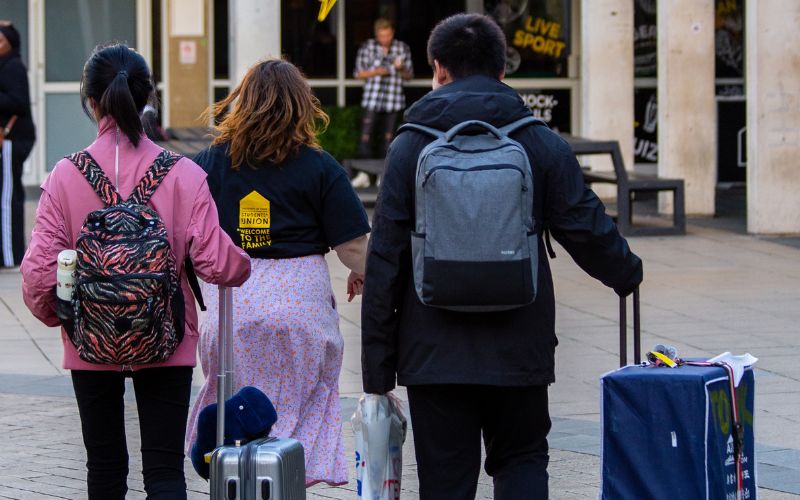 two students with suitcases being lead by an su staff member